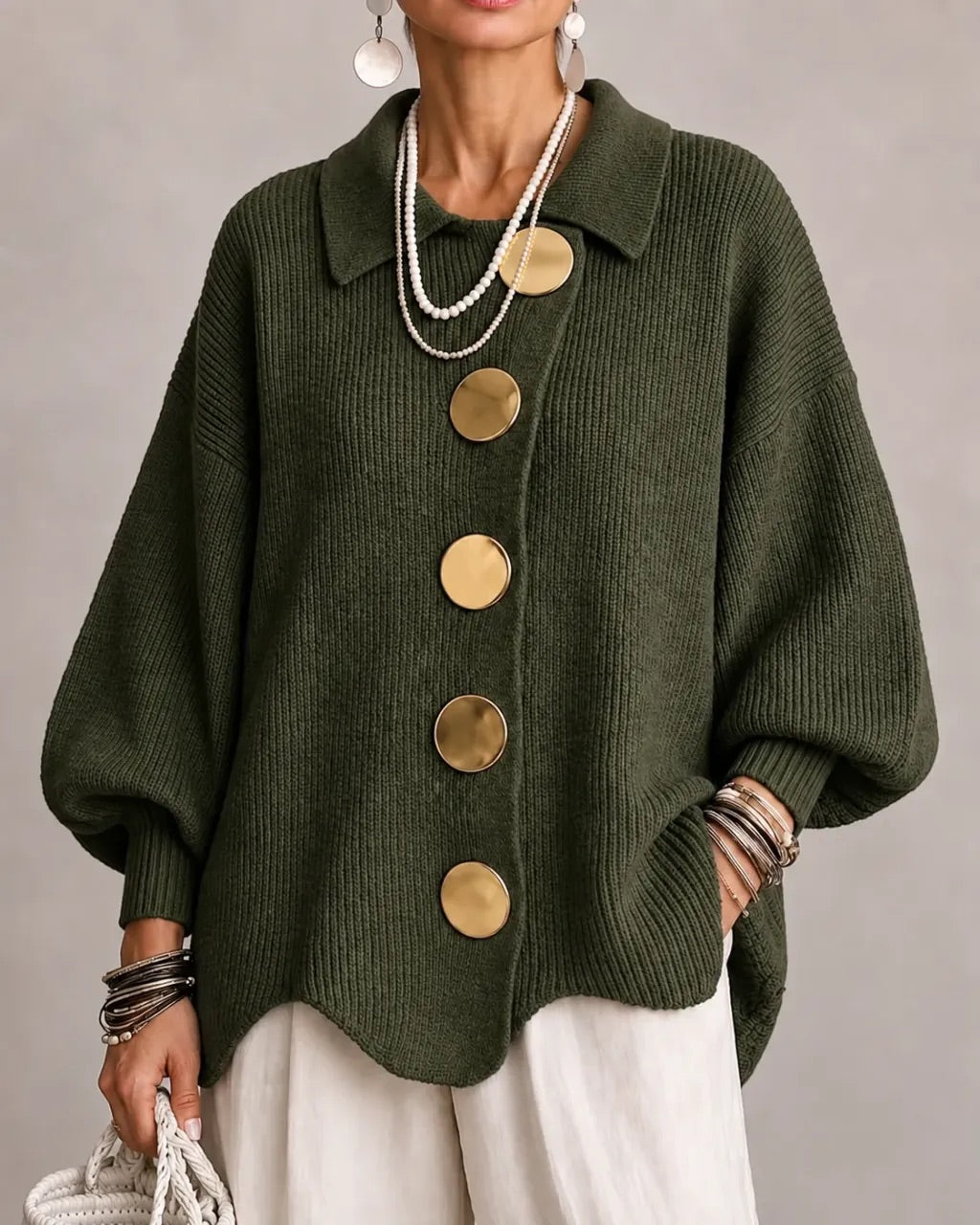 Strickjacke in dunklem Olivgrün mit goldfarbenen Knöpfen, getragen zu weißer Hose, Perlenketten und Armreifen. 12