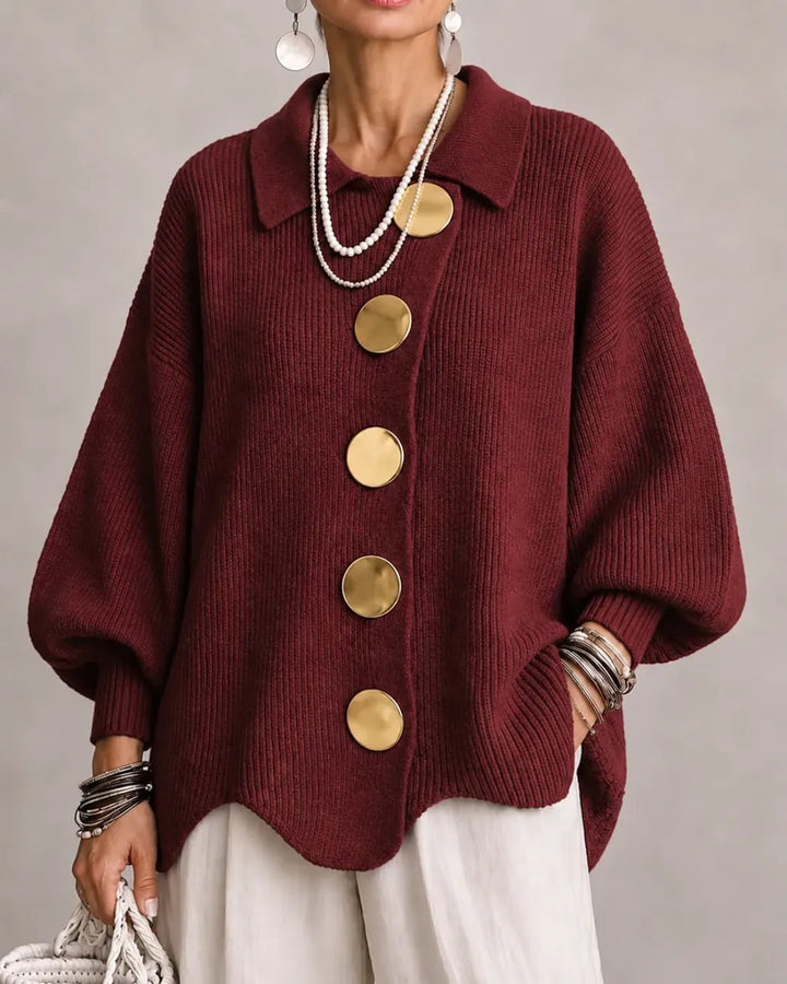 Strickjacke in Weinrot mit goldfarbenen Knöpfen, getragen zu weißer Hose, Perlenketten und Armreifen, Frontansicht. 19