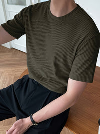 Mann in olivgrünem, geripptem T-Shirt, sitzt an Holztisch, modisch, lässig, Herrenmode.