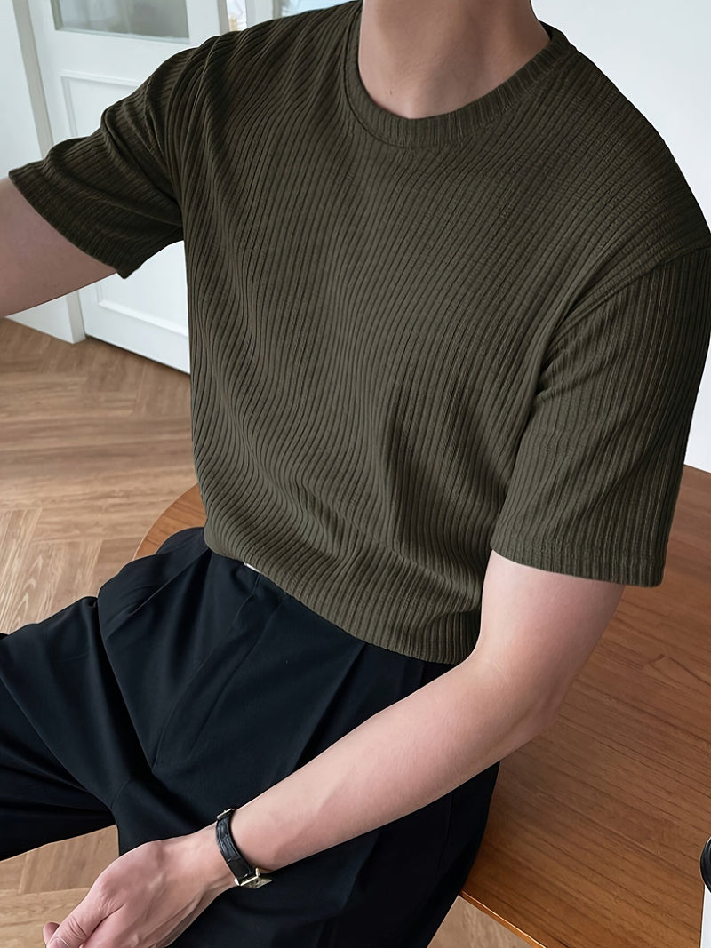 Mann in olivgrünem, geripptem T-Shirt, sitzt an Holztisch, modisch, lässig, Herrenmode.