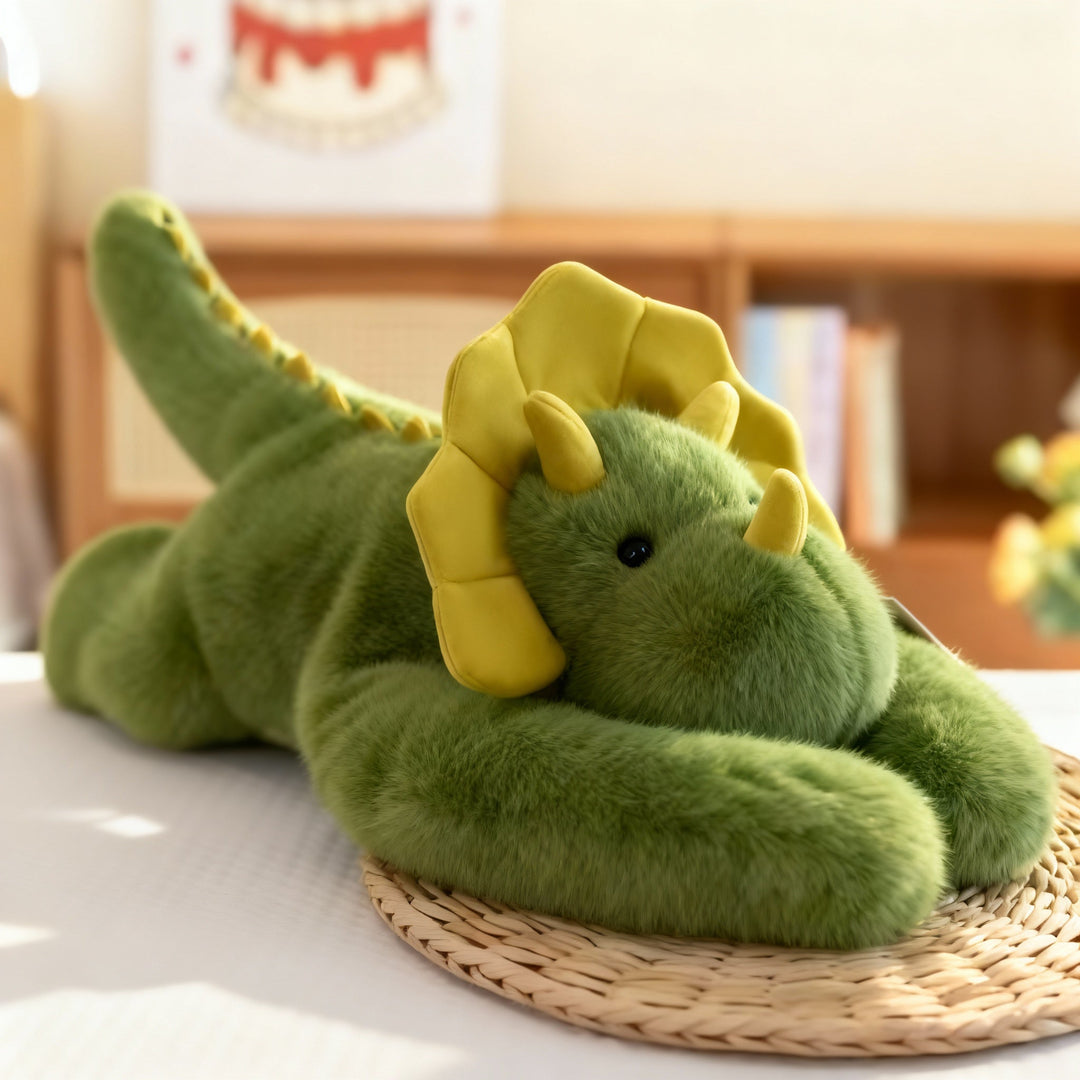 Grünes Drachen-Kuscheltier mit gelbem Nackenschild und gelben Hörnern liegt auf einer Strohmatte, die langen Arme nach vorn gelegt. 15