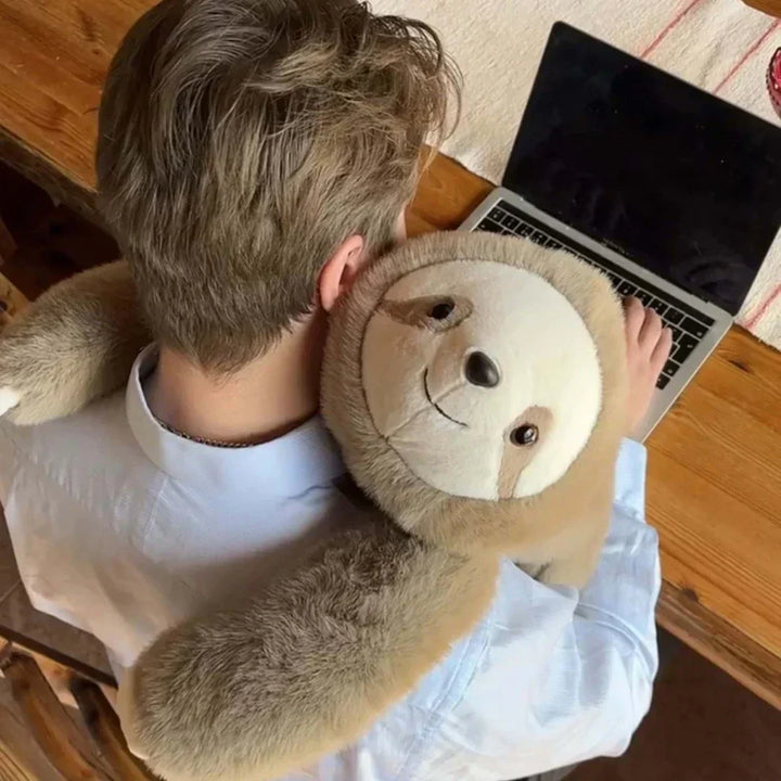 Draufsicht auf eine Person am Laptop, die ein Faultier-Plüschtier mit langen Armen um Schulter und Nacken gelegt hat. 9