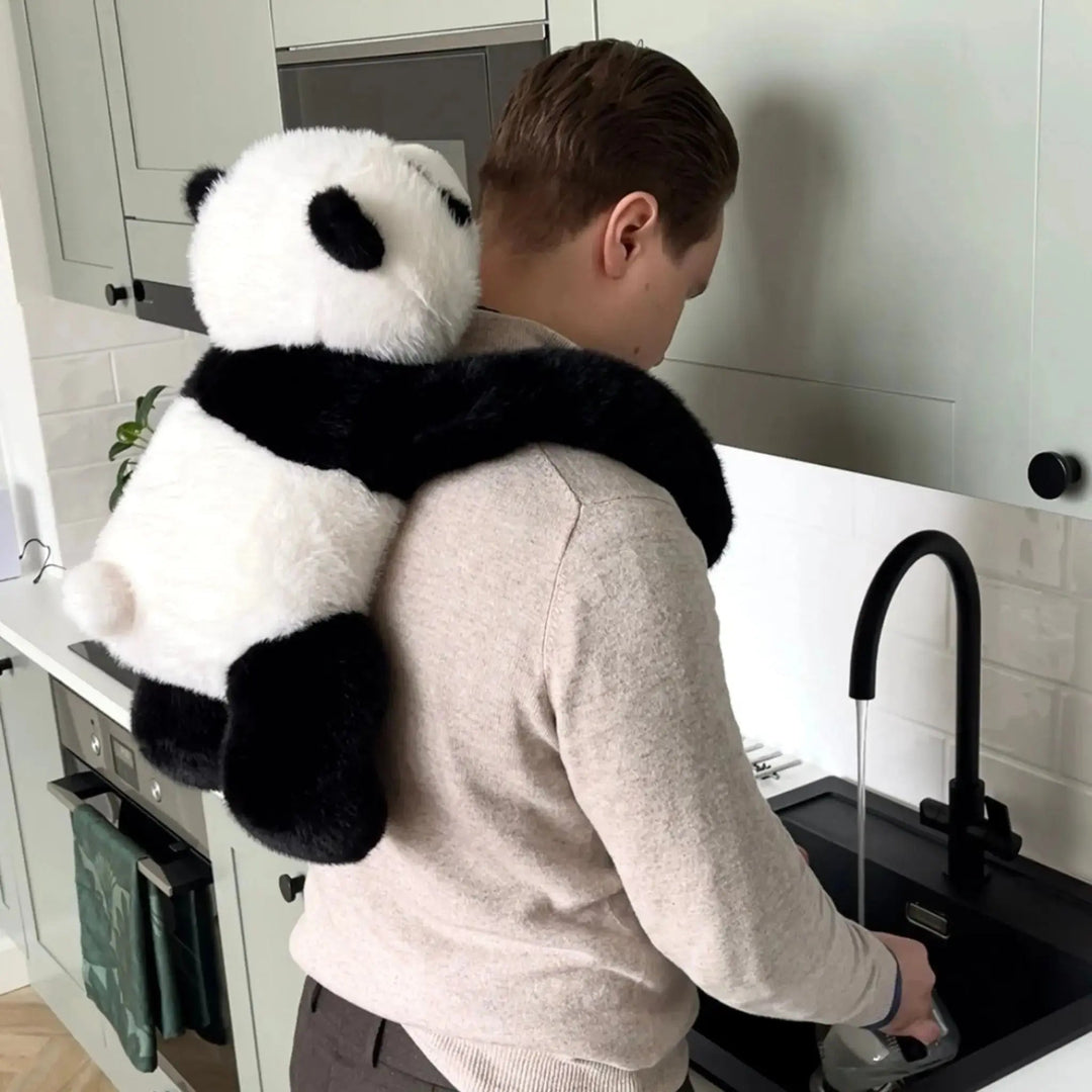 Mann spült in der Küche ab, während der Panda mit seinen langen Armen auf seinen Schultern und dem Rücken hängt. 10
