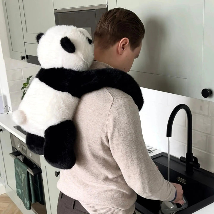 Mann spült in der Küche ab, während der Panda mit seinen langen Armen auf seinen Schultern und dem Rücken hängt. 10
