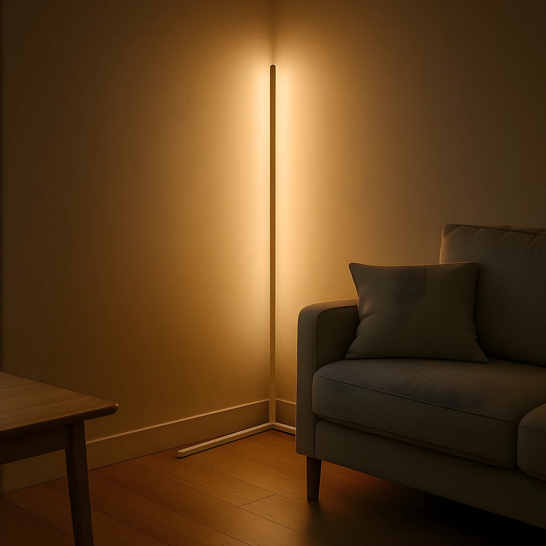 Weiße Variante der Eckleuchte strahlt warmes Licht in die Wandecke, daneben ein Sofa mit Kissen und ein Holztisch. 7