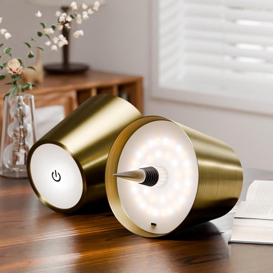 Zwei goldene Lampenaufsätze liegen auf einem Holztisch, einer zeigt die leuchtende LED-Unterseite mit Flaschenstopfen, der andere den Touch-Schalter. 9