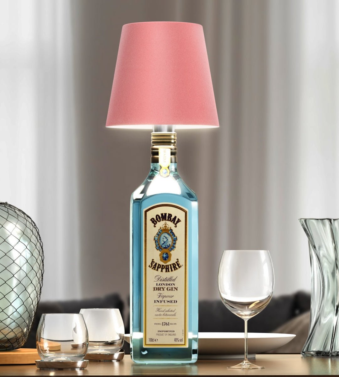 Rosafarbener Lampenschirm auf einer blauen Ginflasche, umgeben von Gläsern und Glasvasen auf einem gedeckten Tisch. 4