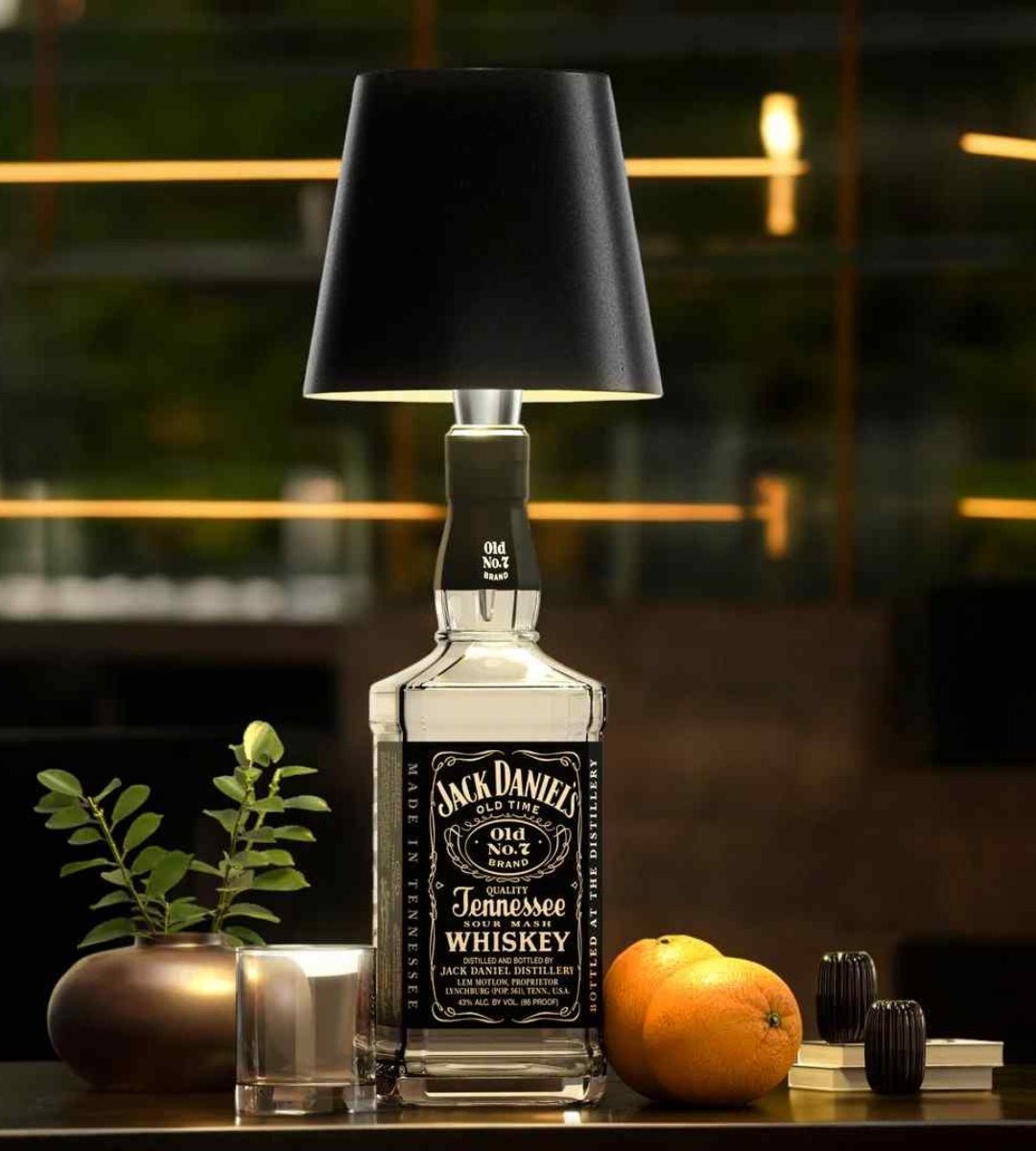 Schwarzer Lampenschirm auf einer klaren Whiskeyflasche, daneben Glas, Orangen und eine Pflanze auf einem Tresen. 2
