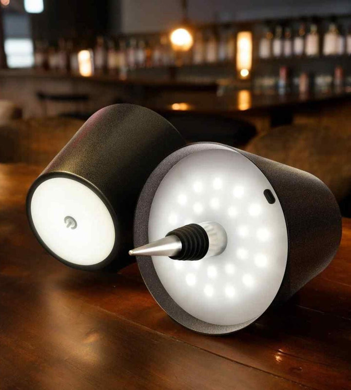 Zwei schwarze Lampenaufsätze auf einem Tresen, die Unterseite mit vielen LEDs und Stopfen leuchtet, der andere zeigt die Touch-Taste. 10