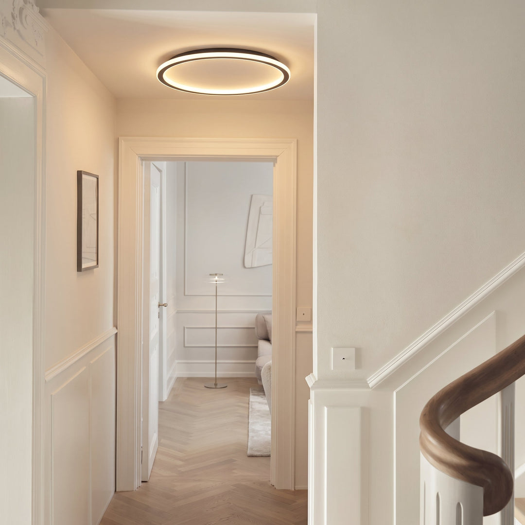 Die Leuchte an der Decke eines hellen Flurs mit weißen Wandpaneelen, Fischgrätparkett und einer Holztreppe. 5