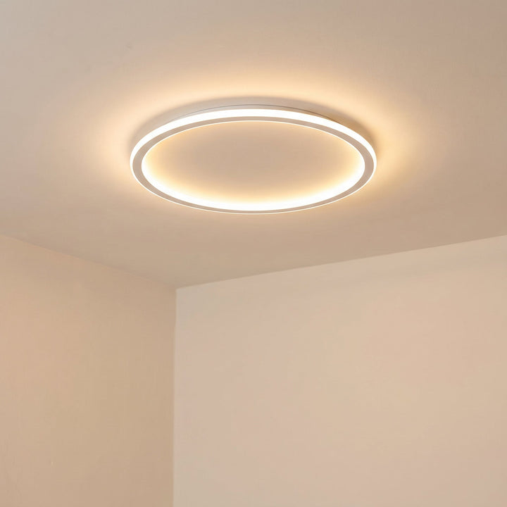 Schräge Ansicht der eingeschalteten Ringleuchte an der Decke vor einer cremefarbenen Raumecke. 6