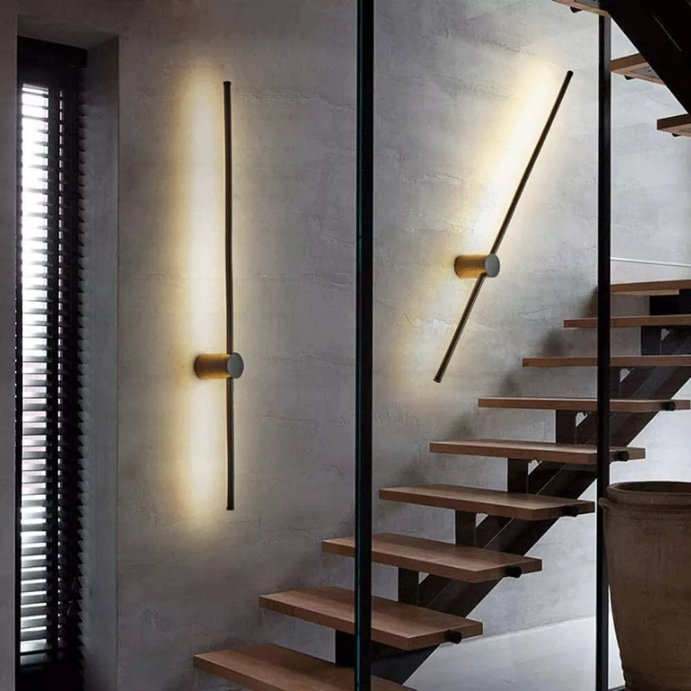 Zwei Leuchtstäbe, einer senkrecht und einer schräg, erhellen eine graue Betonwand neben einer Treppe mit Holzstufen und einer Glasscheibe. 4