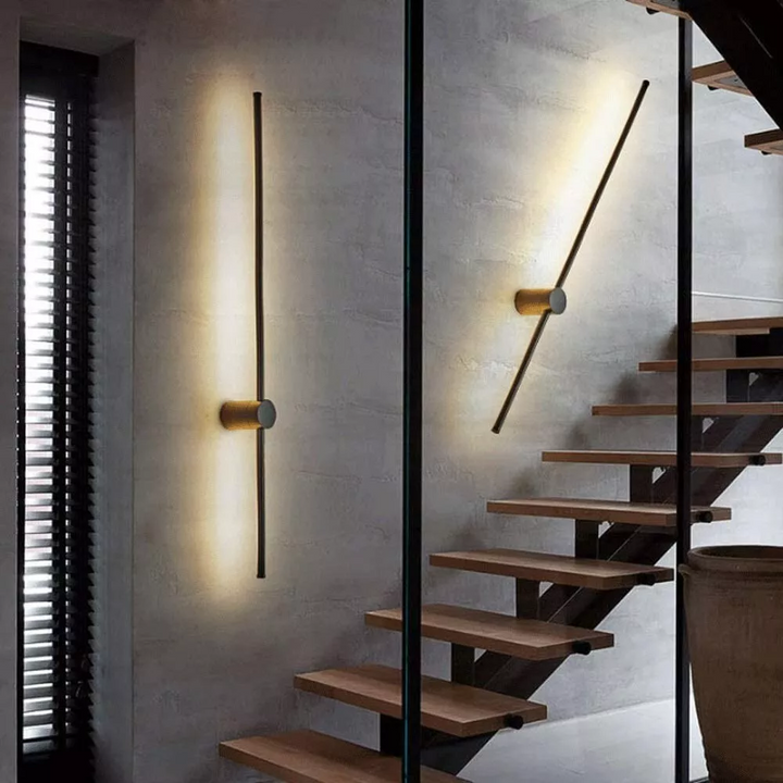 Zwei Leuchtstäbe, einer senkrecht und einer schräg, erhellen eine graue Betonwand neben einer Treppe mit Holzstufen und einer Glasscheibe. 4