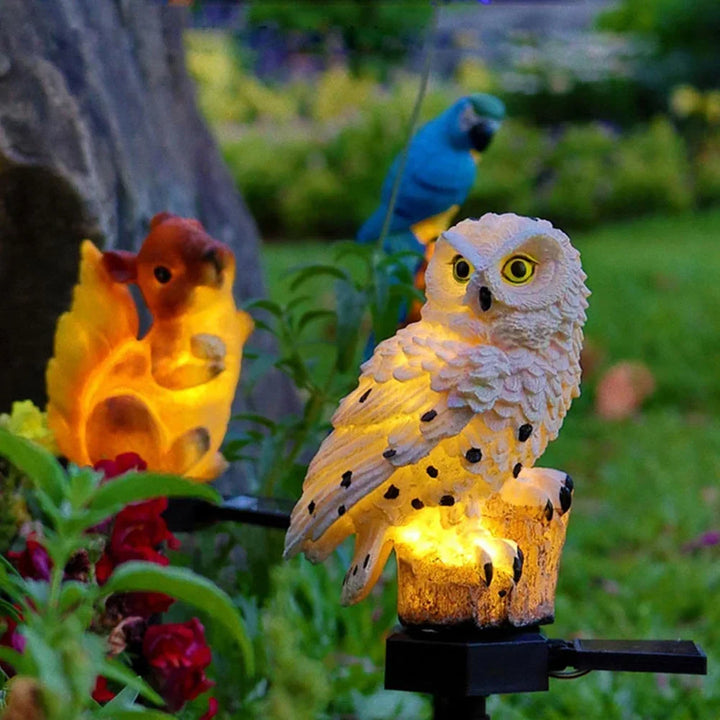 Leuchtende Eule im Garten neben einer orange leuchtenden Eichhörnchenleuchte und einem blauen Papagei im Hintergrund. 12