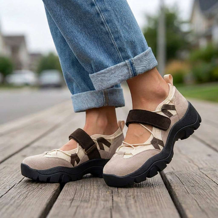 Beige Slipper mit braunem Klettriemen und schwarzer Profilsohle, getragen mit umgeschlagener Jeans auf einem Holzsteg in einer Wohnstraße. 6