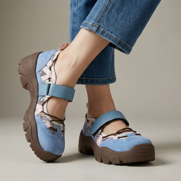 Hellblaue Veloursleder-Slipper mit blauem Klettriemen, kariertem Einsatz, rosa Bändern und brauner Profilsohle, getragen mit heller Jeans im Studio. 3