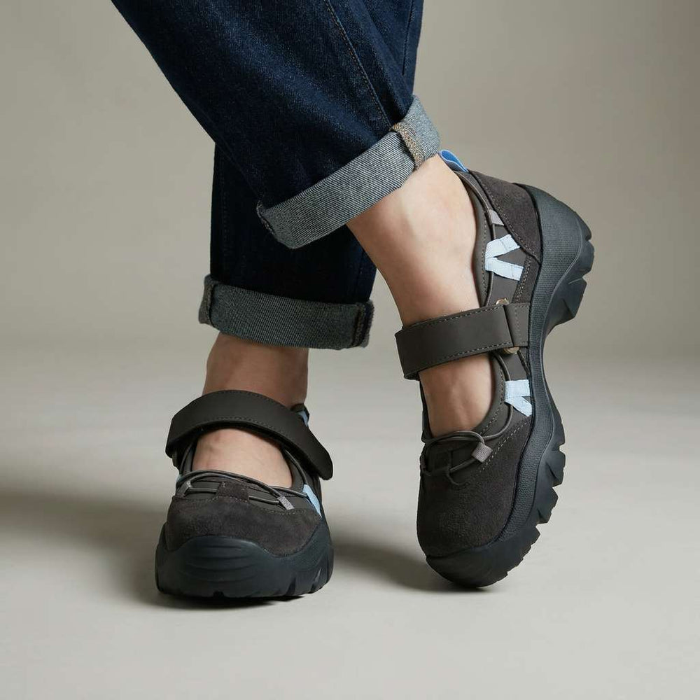Dunkelgraue Slipper mit Klettriemen, hellblauen Zierbändern und schwarzer Profilsohle, getragen mit umgeschlagener dunkler Jeans im Studio. 2