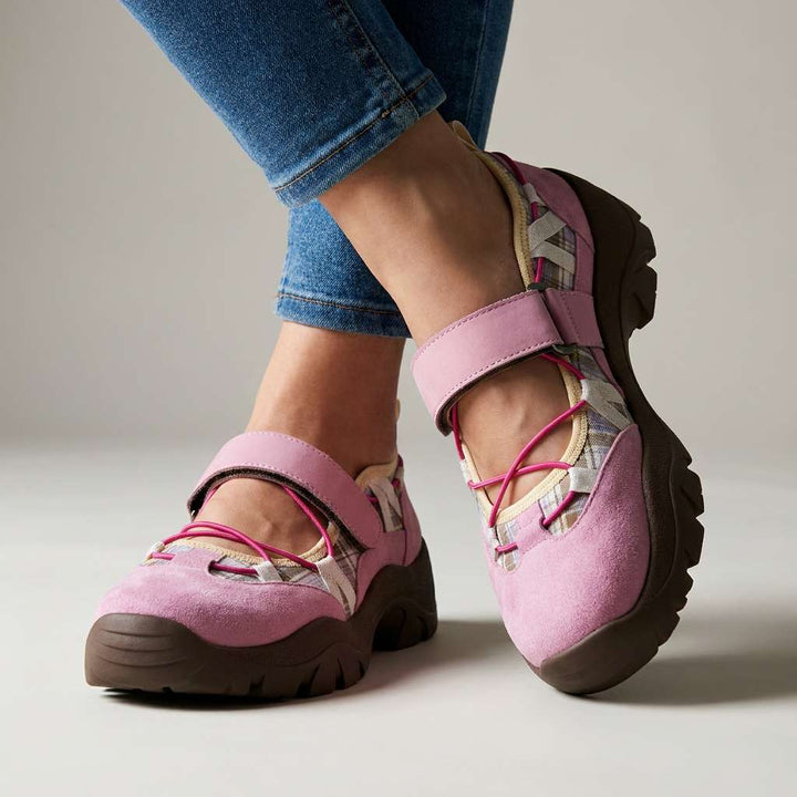 Rosa Veloursleder-Slipper mit Klettriemen, pinkfarbenen Gummizügen, kariertem Einsatz und brauner Profilsohle, getragen mit Jeans im Studio. 4