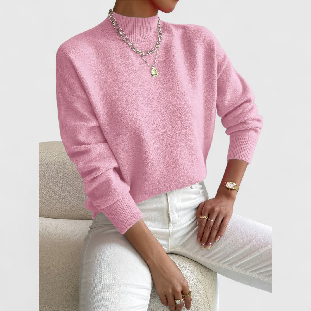 Rosa Pullover mit Stehkragen am Model, kombiniert mit weißer Hose, silbernen Ketten und goldener Armbanduhr vor hellem Hintergrund. 5