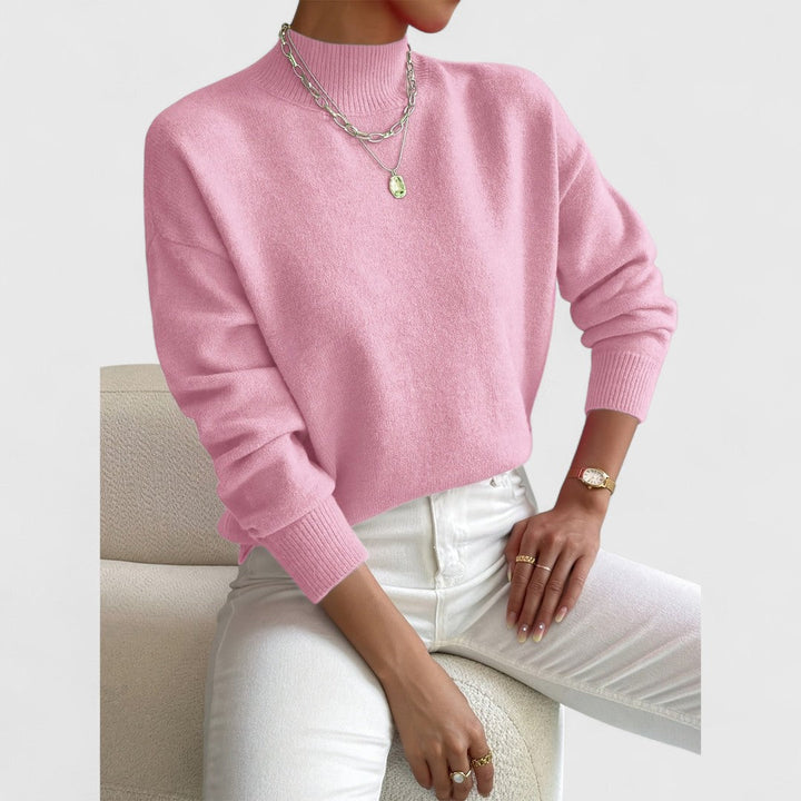 Rosa Pullover mit Stehkragen am Model, kombiniert mit weißer Hose, silbernen Ketten und goldener Armbanduhr vor hellem Hintergrund. 5