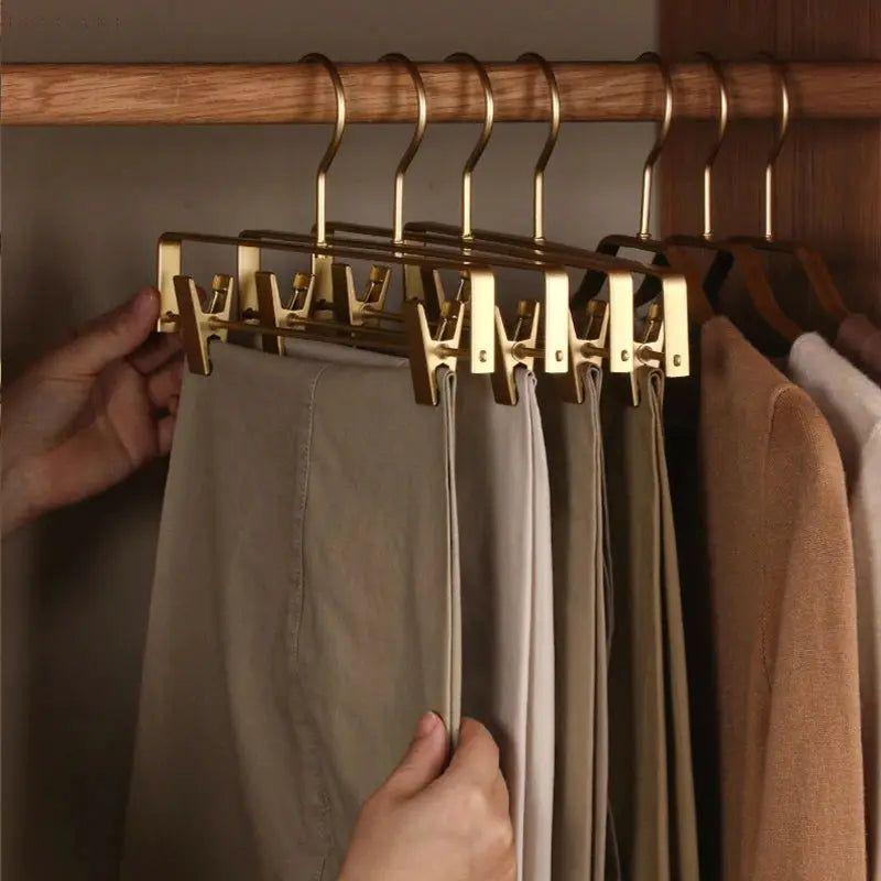 Hand zieht eine beige Hose von goldfarbenen Klammerbügeln an der Kleiderstange im Holzschrank 7