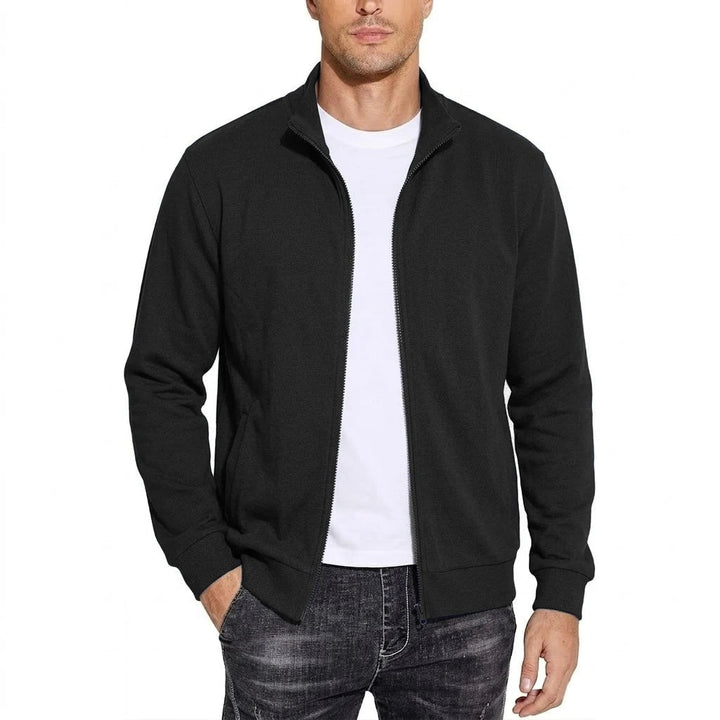 Frontansicht der schwarzen Sweatshirt-Jacke mit Stehkragen, offen getragen über weißem T-Shirt, Hand in der Tasche. 1