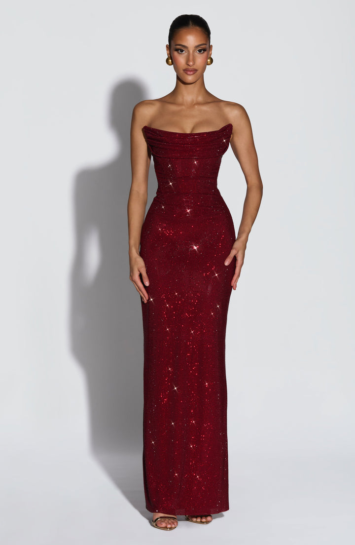 Model trägt das trägerlose Maxikleid in Dunkelrot mit Strassbesatz in der Frontansicht, mit drapiertem Mieder und goldenen Ohrringen. 1