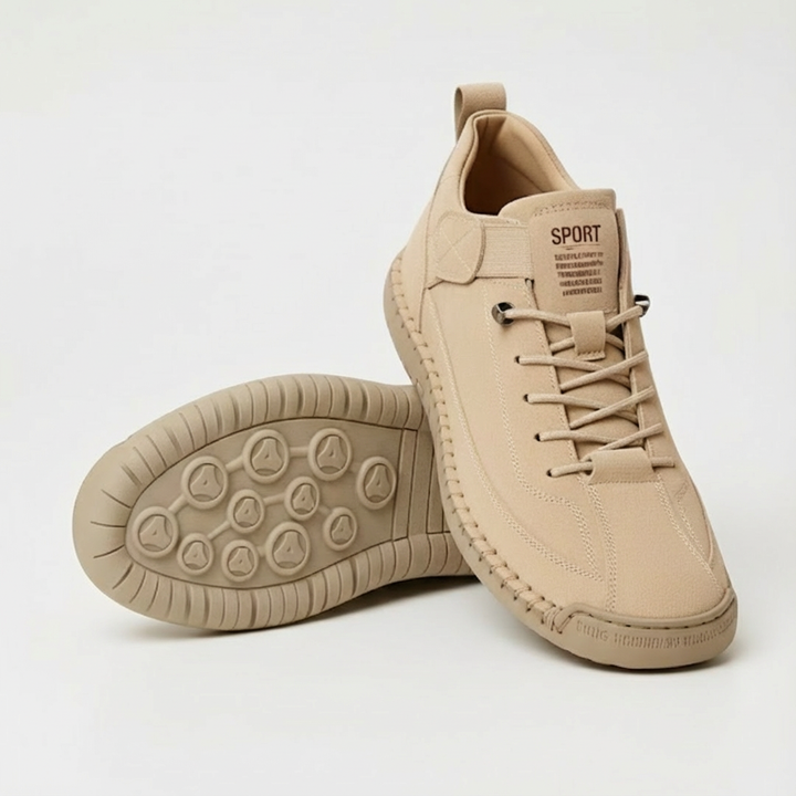 Beiger Sneaker aus Veloursleder-Optik mit Schnürung, daneben ein zweiter Schuh mit der profilierten Laufsohle nach oben, heller Hintergrund. 1