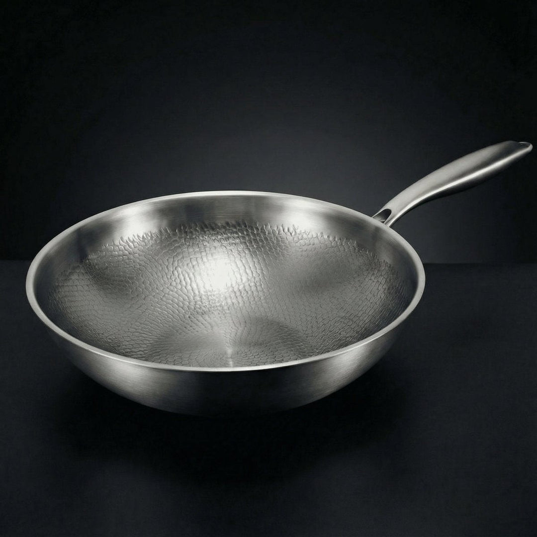Wokpfanne aus Metall mit gehämmerter Innenfläche und langem Stielgriff, schräg von oben vor dunklem Hintergrund fotografiert. 1