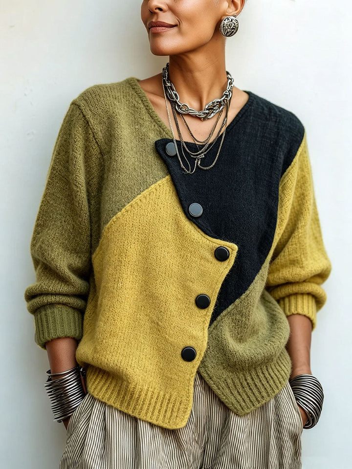 Frontansicht an einer Frau vor heller Wand: Strickpullover in Oliv, Gelb und Schwarz mit schräger Knopfleiste, kombiniert mit Kettenschmuck und gestreifter Hose 1