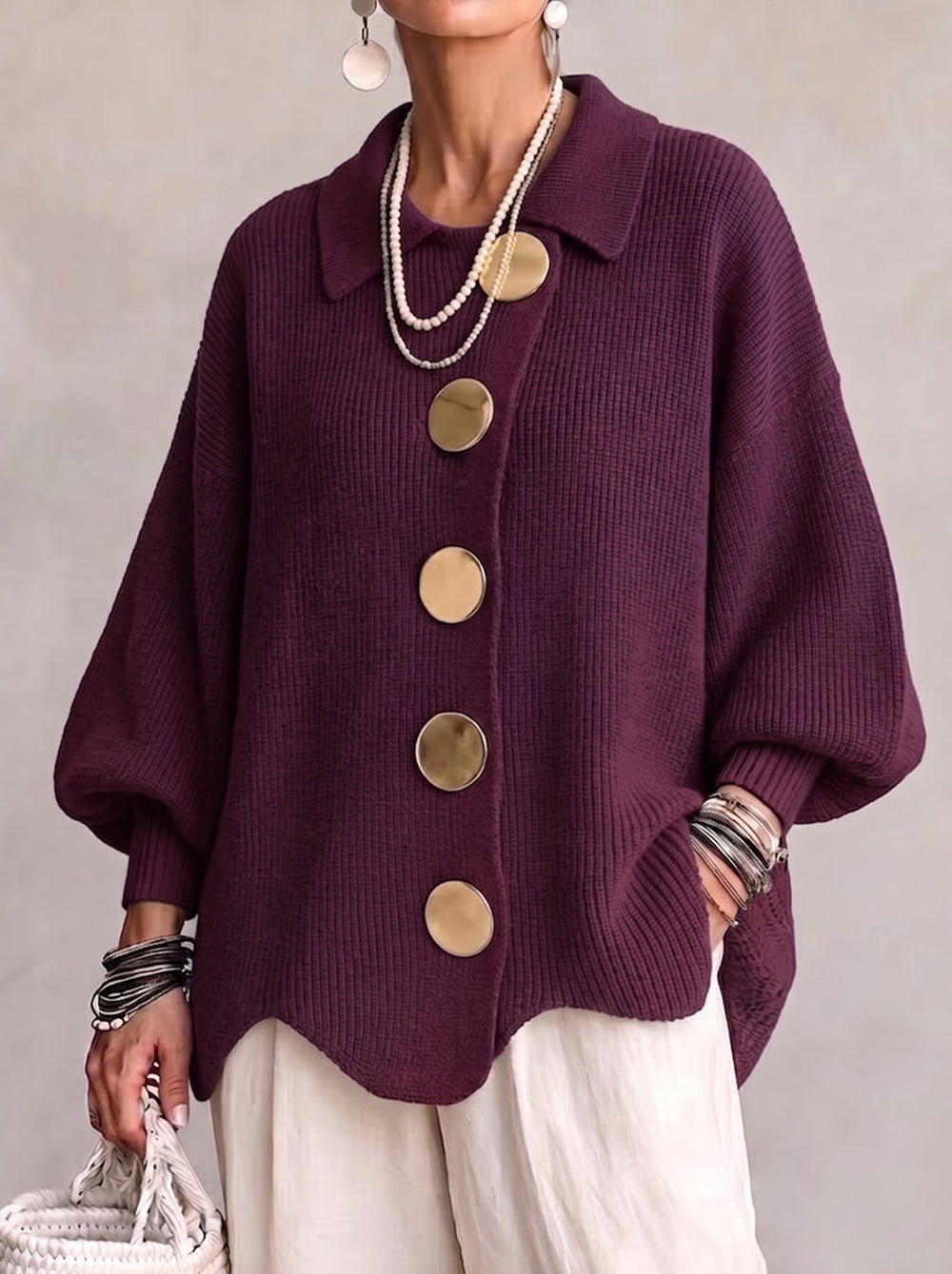 Frontansicht der Strickjacke in dunklem Beerenviolett, getragen mit Perlenketten, heller Leinenhose und weißer Korbtasche. 2