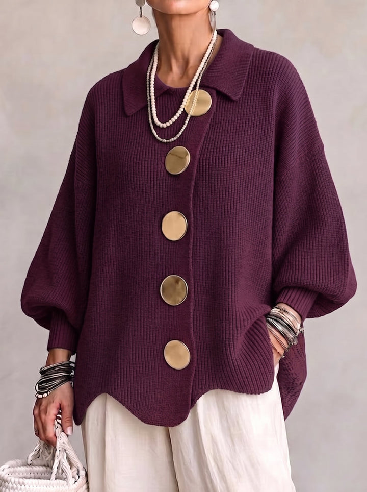 Frontansicht der Strickjacke in dunklem Beerenviolett, getragen mit Perlenketten, heller Leinenhose und weißer Korbtasche. 2