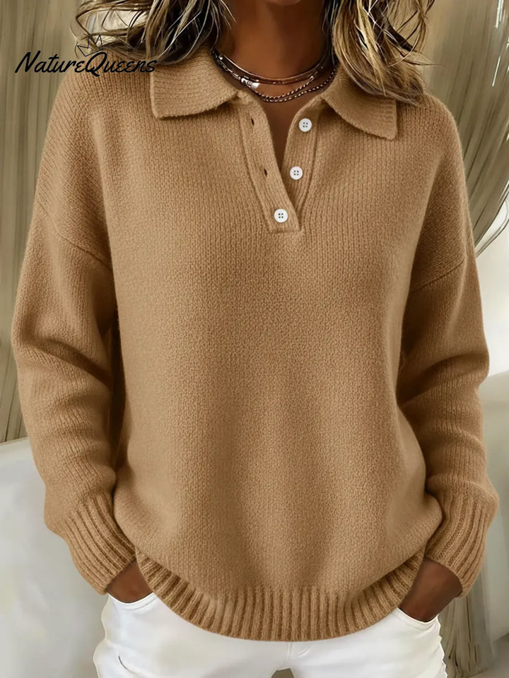 Frau trägt den Strickpullover in Camelbraun, Vorderansicht mit Polokragen, weißen Knöpfen und geripptem Saum, die Hände in den Taschen. 4
