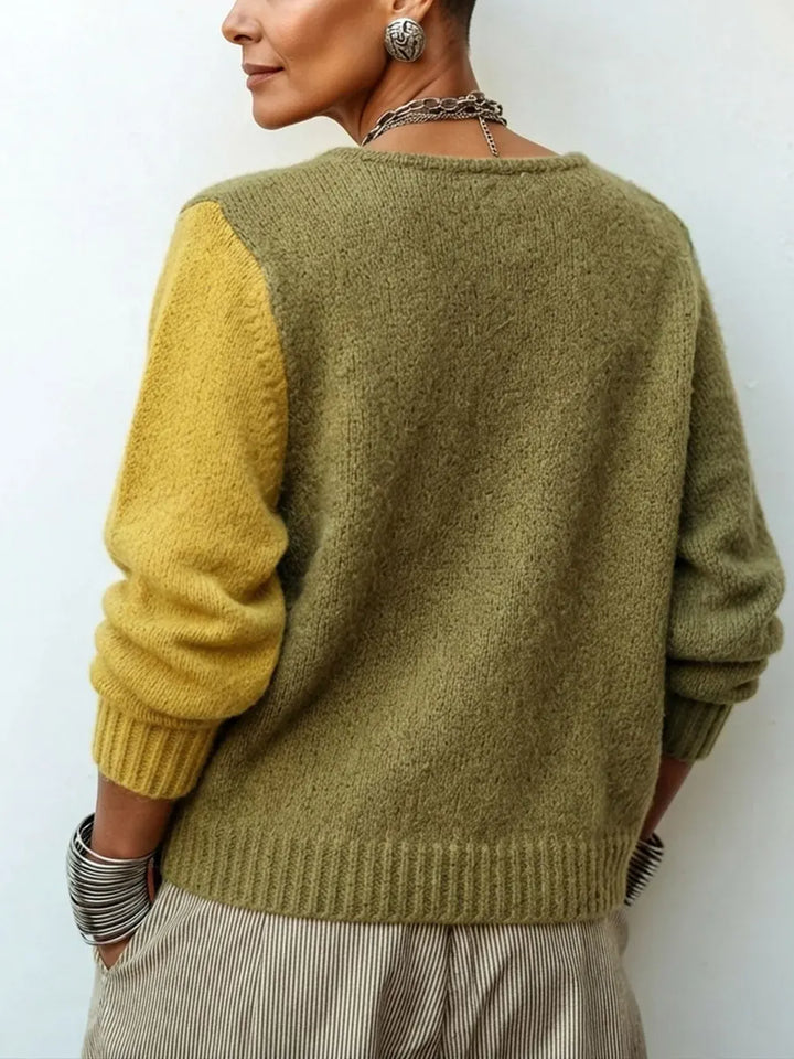Rückansicht des Pullovers an einer Frau: grünes Rückenteil mit einem gelben Ärmel und gerippten Bündchen, dazu gestreifte Hose. 2