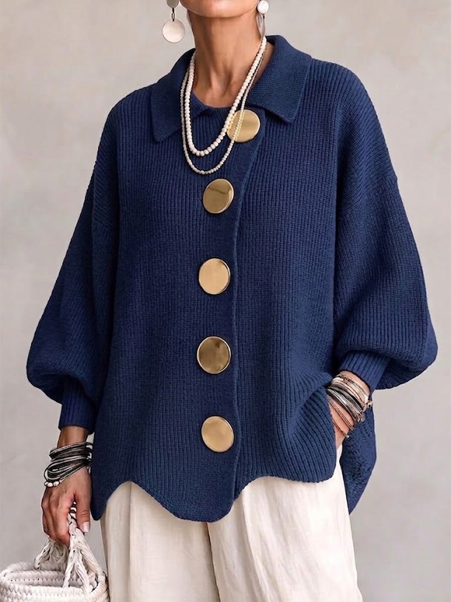 Frau trägt die Strickjacke in Marineblau mit großen goldfarbenen Knöpfen, Perlenketten und heller Hose, Frontansicht. 1