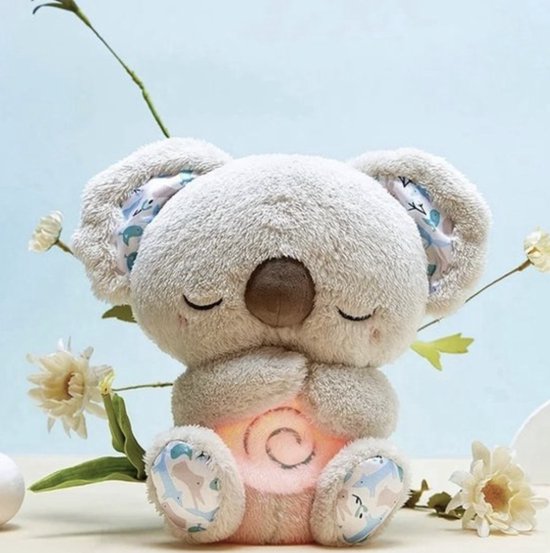 Graues Koala-Plüschtier mit geschlossenen Augen und gefalteten Pfoten, leuchtendem Spiralmuster am Bauch, umgeben von weißen Blumen. 1