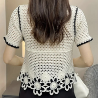 Rückansicht einer Frau in weißer, gehäkelter Spitzenbluse mit Blumenmuster, schwarz umrandet.
