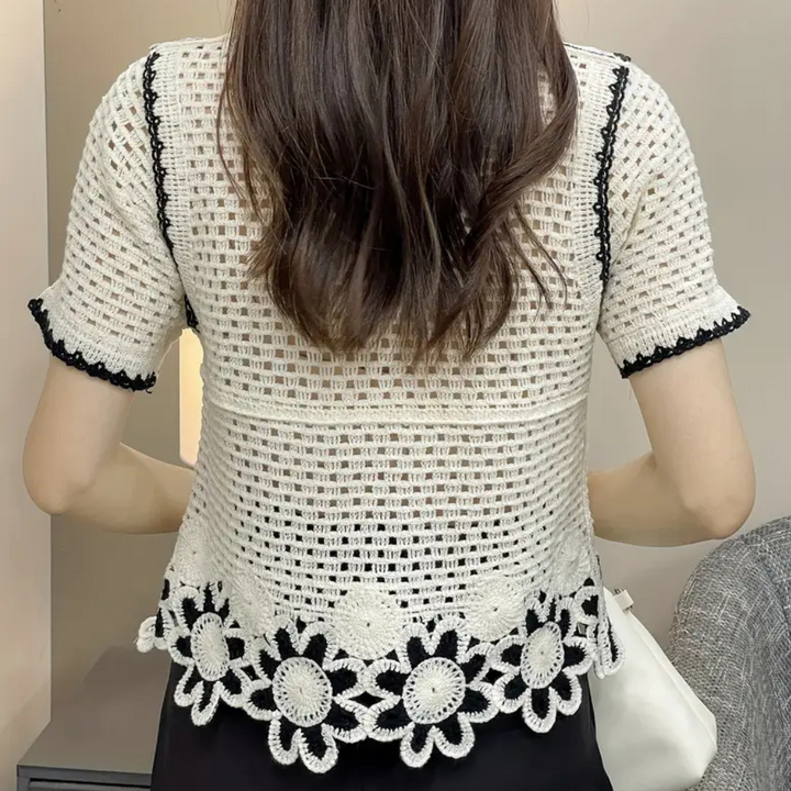Rückansicht einer Frau in weißer, gehäkelter Spitzenbluse mit Blumenmuster, schwarz umrandet.