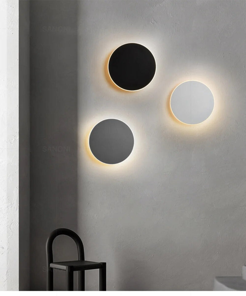 Drei runde LED-Wandlampen in Schwarz, Grau und Weiß an grauer Wand, modernes Design.