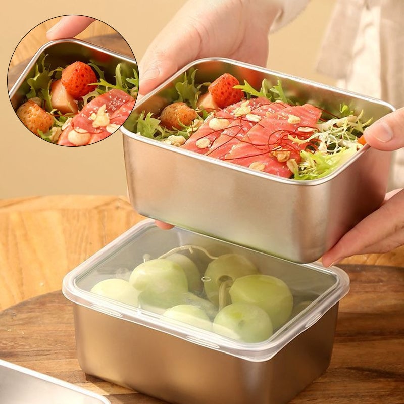 Hände halten eine Edelstahlbox mit Salat, Lachs und Erdbeeren über einer zweiten Box mit transparentem Deckel und grünen Trauben, Detailausschnitt links. 1