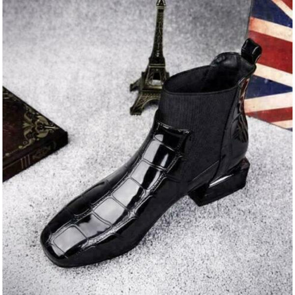 Schwarzer Stiefel mit glänzender Krokooptik und quadratischer Spitze, schräg von oben vor dekorativem Hintergrund mit Eiffelturm-Figur fotografiert. 7