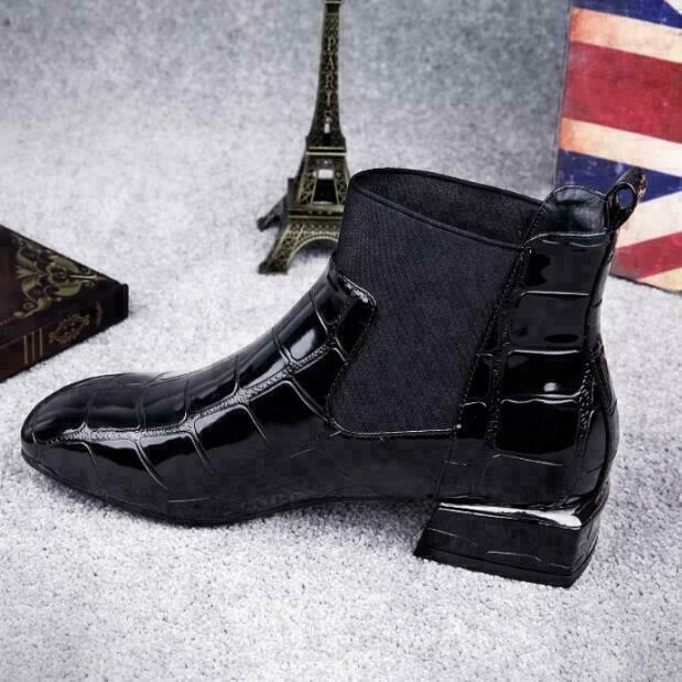 Seitenansicht des glänzenden schwarzen Stiefels mit breitem elastischem Einsatz und flachem Blockabsatz auf grauem Flauschteppich. 6