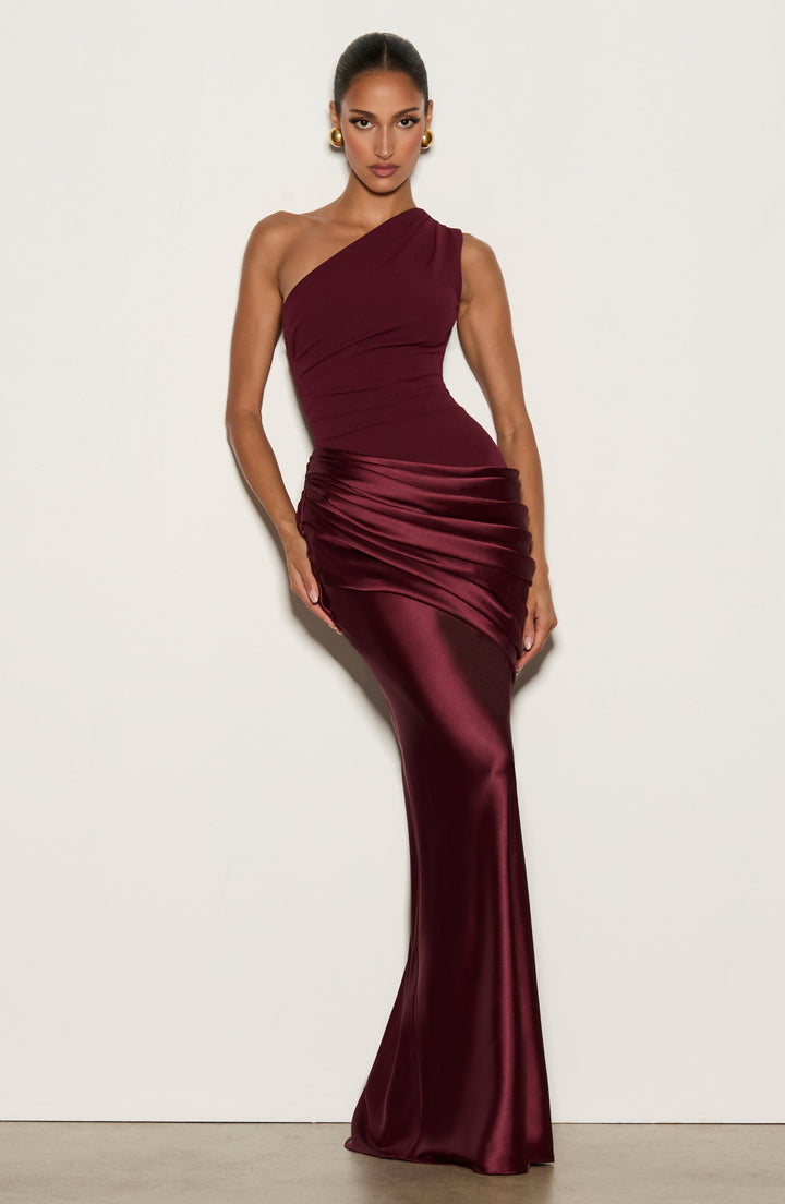 Frau im weinroten Maxikleid vor heller Wand, Pose mit Hand an der Hüfte, glänzender Satin und Hüftdrapé gut sichtbar. 16