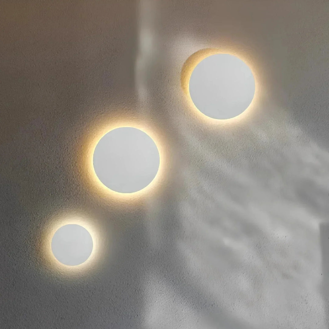 Drei runde weiße Wandleuchten in unterschiedlichen Größen, deren warmes Licht als sanfter Ring an der Wand leuchtet. 4