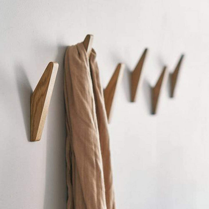 Sechs Holzhaken hängen in einer Reihe an einer weißen Wand, am ersten Haken hängt ein beigefarbener Schal. 2