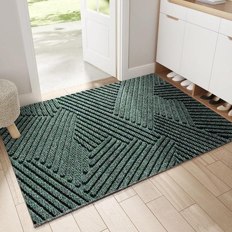 Dunkelgrüne Fußmatte mit erhabenem geometrischem Streifenmuster im Eingangsbereich, neben Schuhschrank und offener Tür auf Holzboden. 1