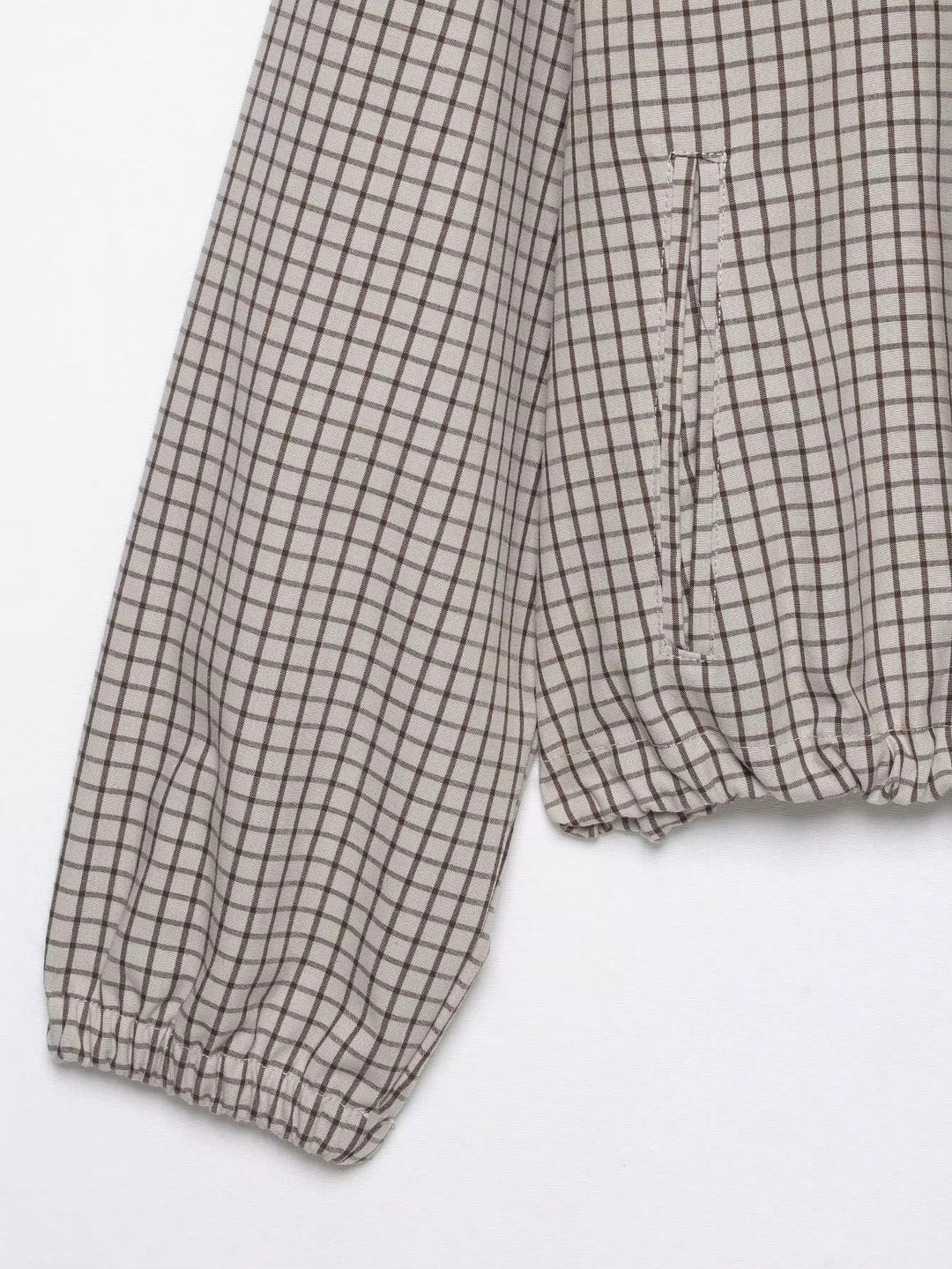 Detail von Ärmel und Saum: Gummibündchen am Ärmelende, seitliche Eingriffstasche und gerafftes Saumband der karierten Jacke auf weißem Grund. 8