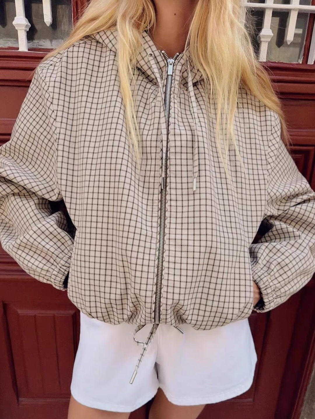 Nahaufnahme der Vorderseite am Model: Reißverschluss, Kapuzenkordeln und Kordelzug am Saum der karierten Jacke, Hände in den Taschen. 3