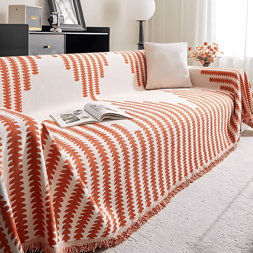 Sofabezug in Weiß mit orange-roten Blattstreifen und Fransenkante, über das Sofa gelegt, mit Magazin und hellem Kissen. 7