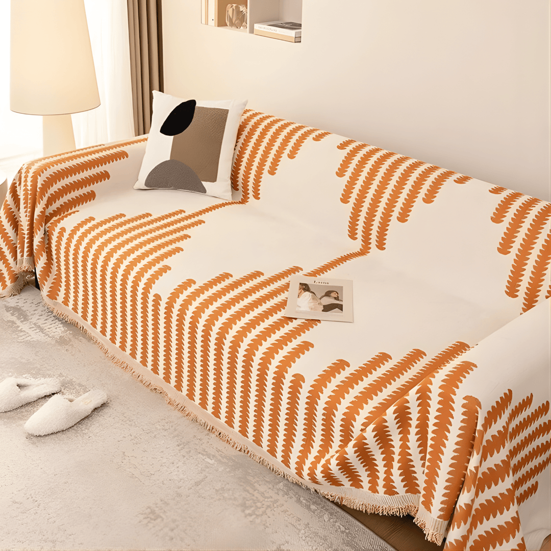 Cremeweißer Sofabezug mit orangefarbenem Blattmuster und Fransenkante, schräg von oben auf dem Sofa fotografiert. 4